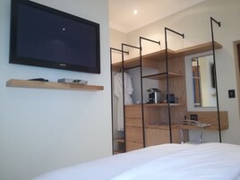 A modern bedroom with a bed, a TV mounted on the wall, a wooden shelf with a clock, and a mirror above a dresser.