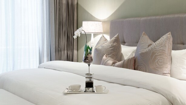 A neatly made bed with white linens, a tray with a teapot and cups, and a potted orchid. - Sugar Hotel (Cape Town)