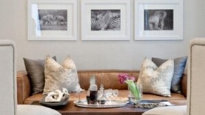 A living room with a brown leather sofa, two armchairs, a coffee table with decorative items, and a wall with six framed photographs. - Sugar Hotel (Cape Town)