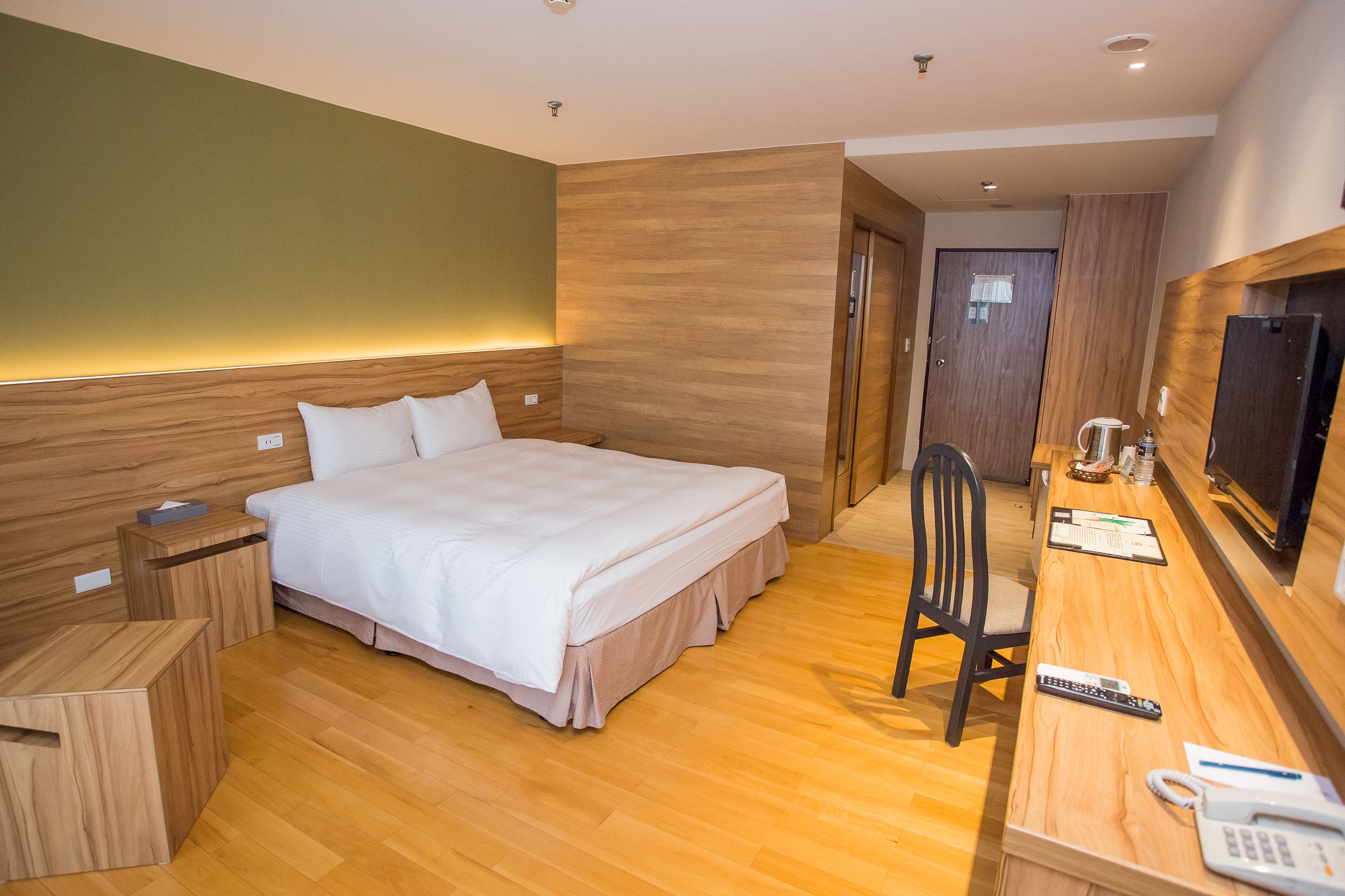 Une chambre d’hôtel avec un lit en bois, un bureau avec une chaise, une télévision et un téléphone.