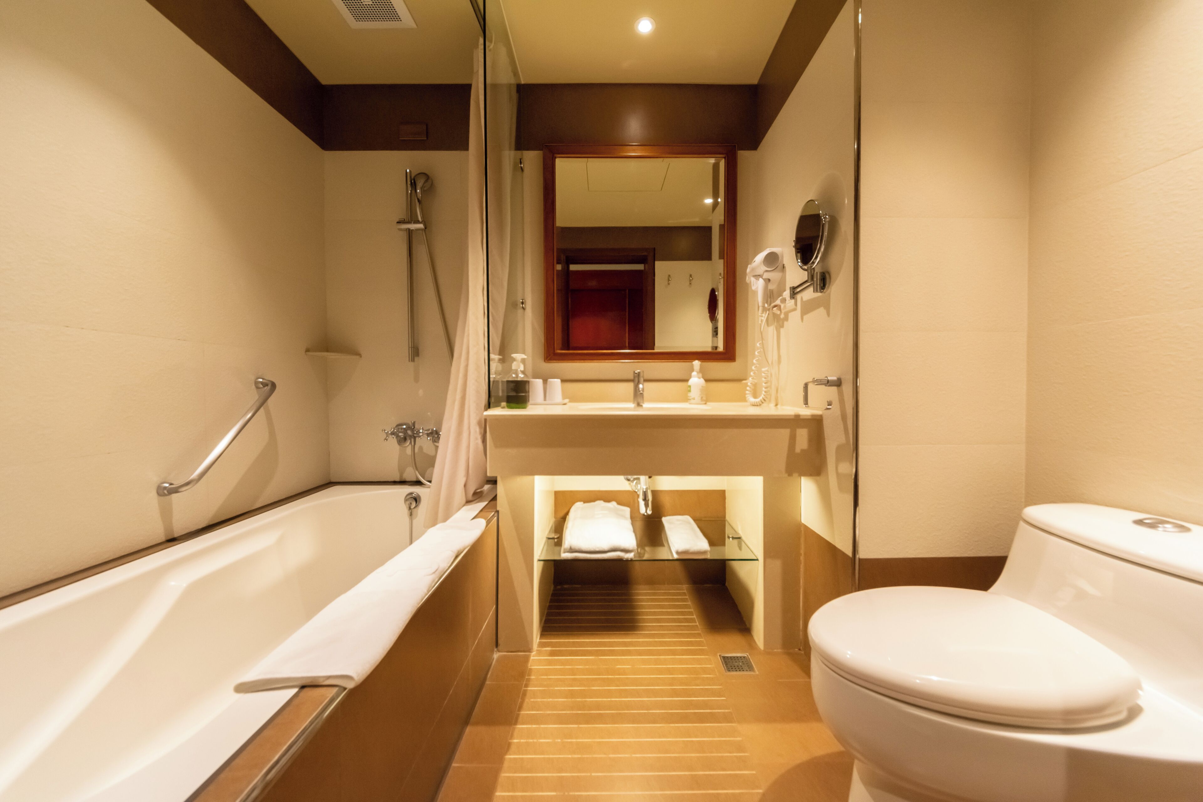 Une salle de bain équipée d’une baignoire, d’un lavabo, de toilettes, d’une douche, d’une étagère en verre et d’un miroir.