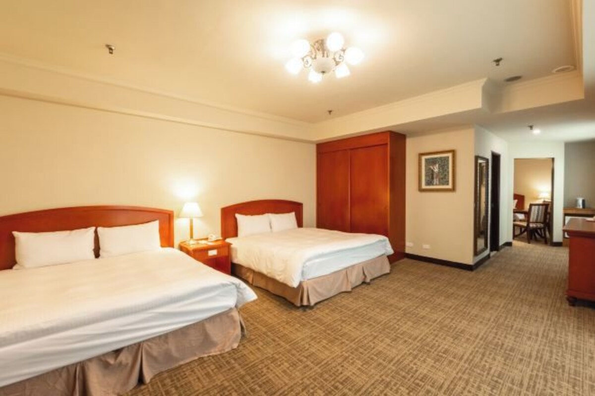 A hotel room with two beds, a desk, a chair, and a wardrobe.