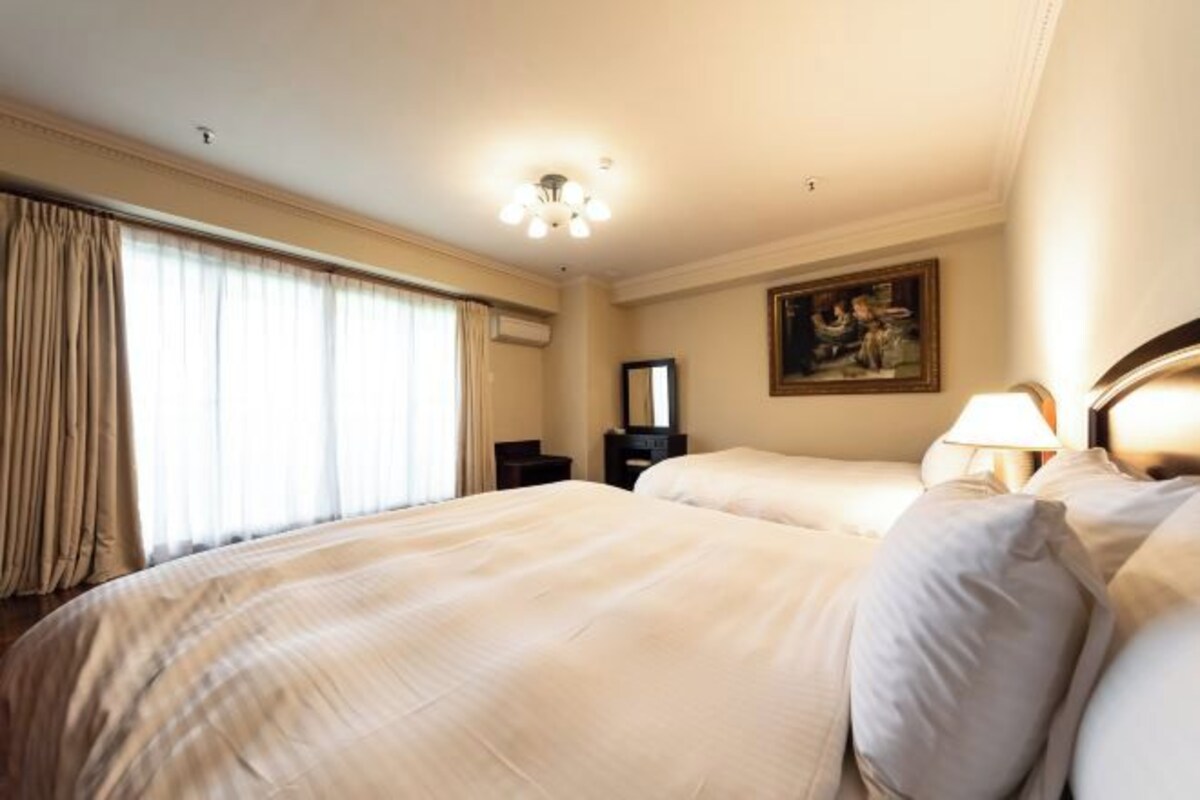 A hotel room with a large bed, a desk, a chair, a lamp, and a painting on the wall.