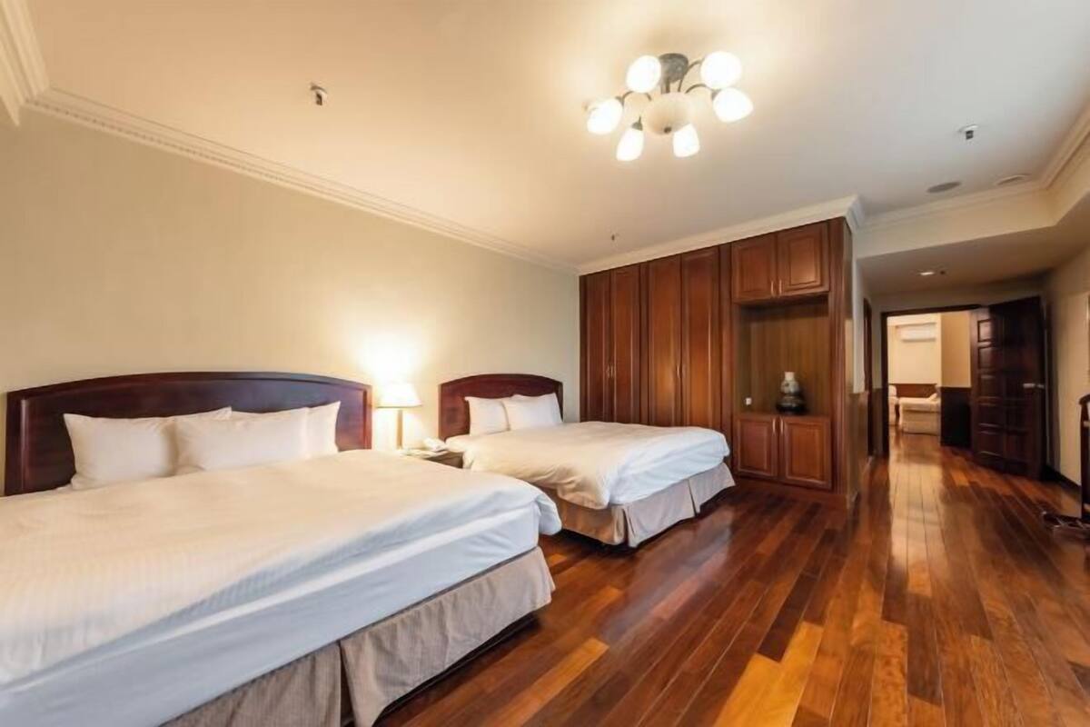 A hotel room with two beds, wooden flooring, a wardrobe, and a chandelier.