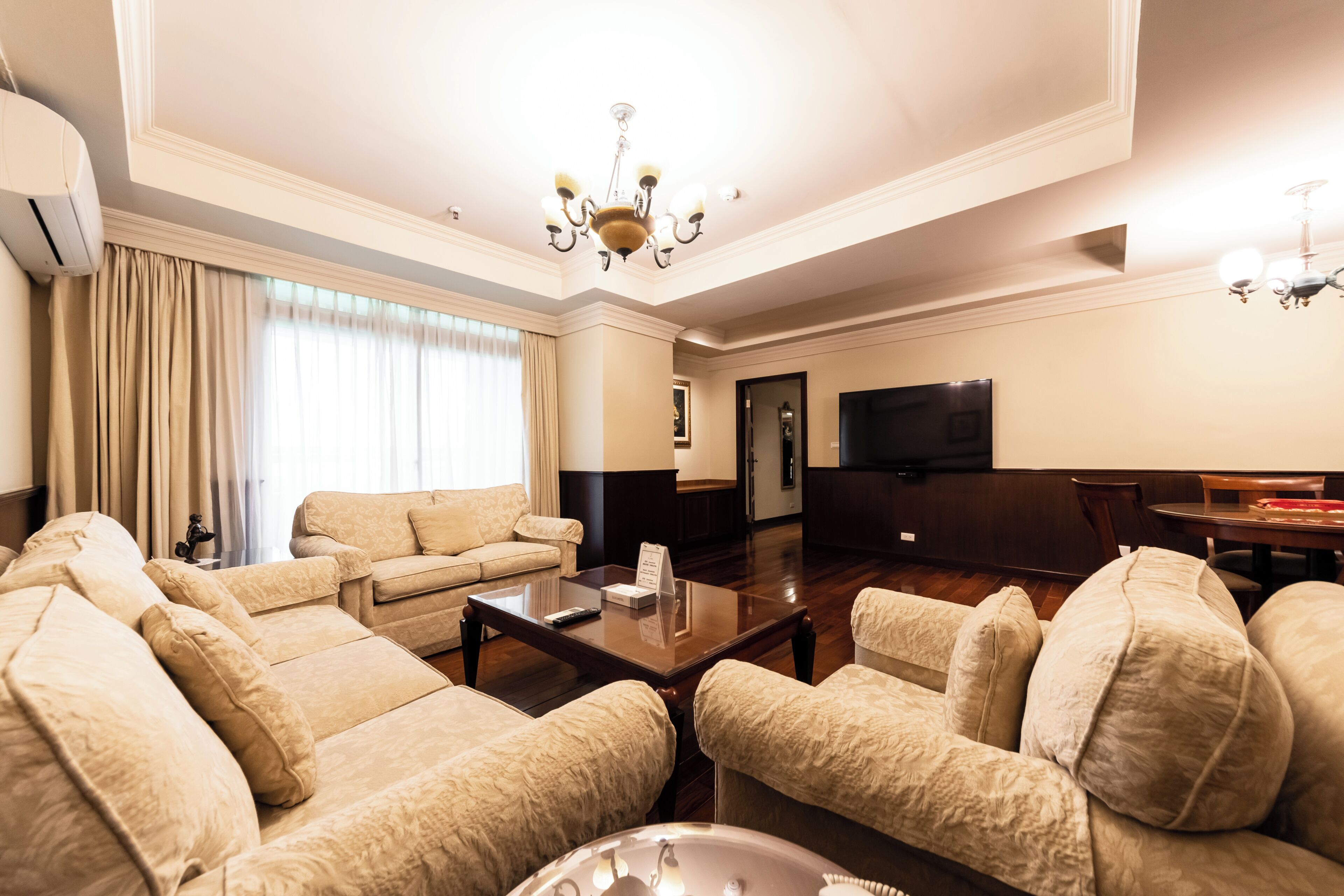 A spacious living room with a large flat-screen TV, a chandelier, and a dining area with a table and chairs.