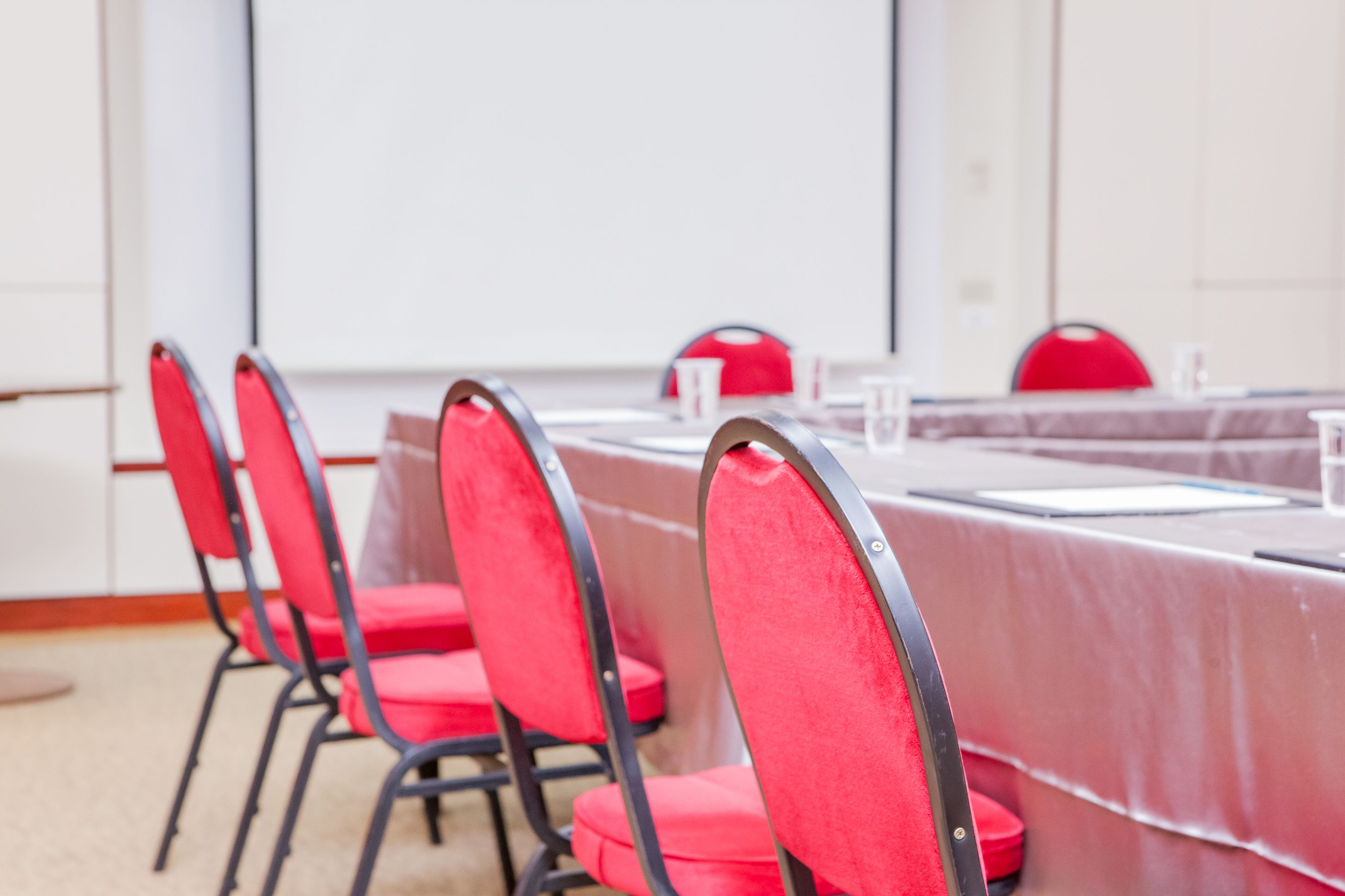 A conference room with a long table, red chairs, and a whiteboard.