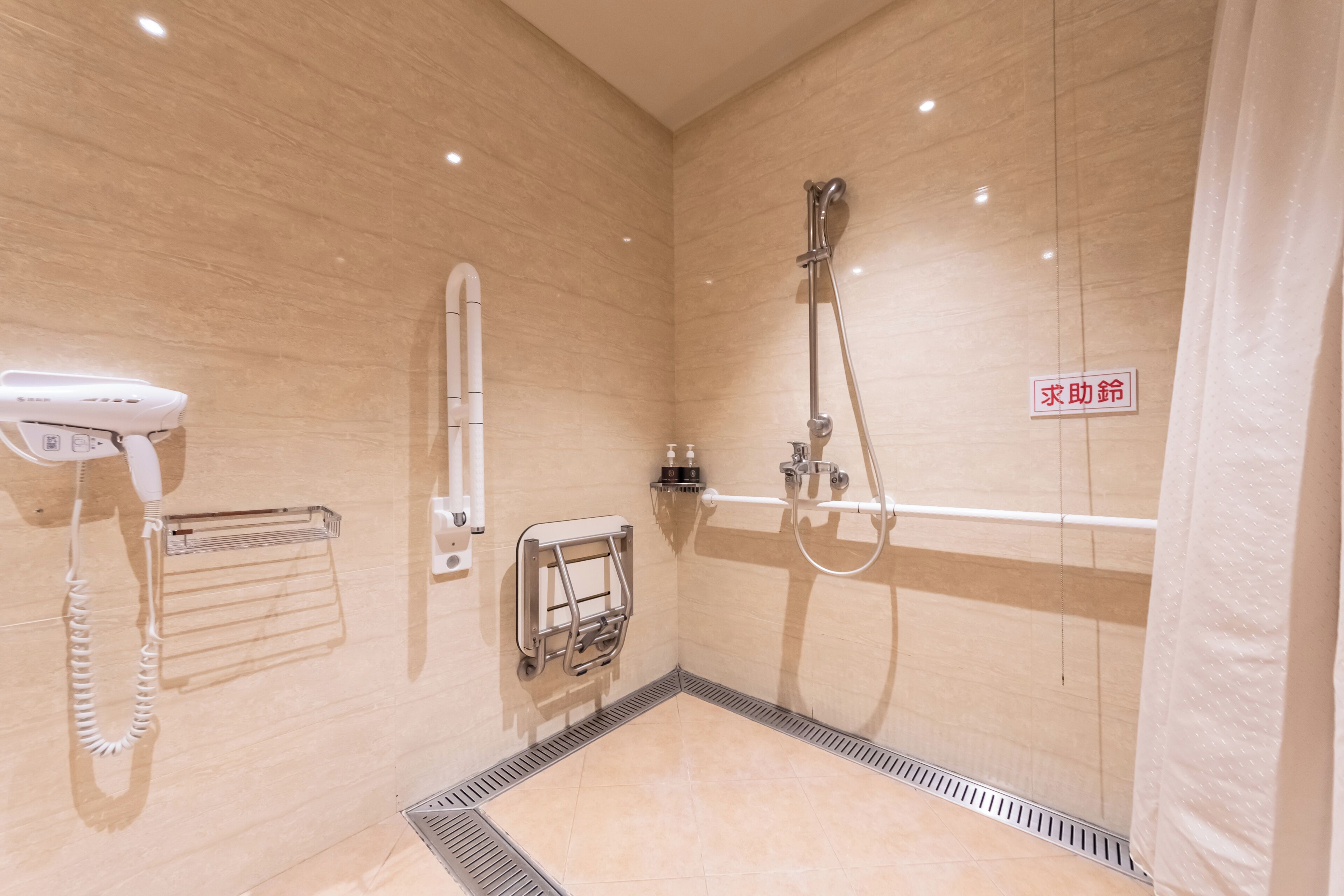 Un baño moderno con ducha, secamanos, toallero y un cartel en idioma extranjero.