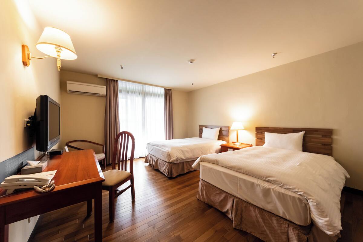 A hotel room with two beds, a desk with a telephone, a television, and a lamp.