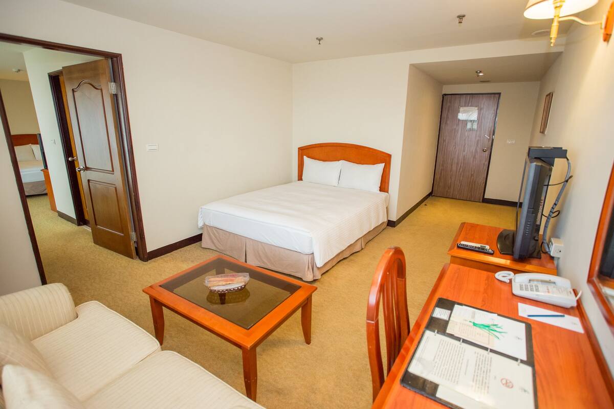 A hotel room with a bed, a desk with a computer, a chair, and a sofa.