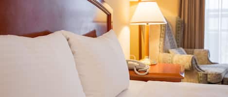 A hotel room with a large bed, a bedside lamp, a telephone, and a patterned armchair.