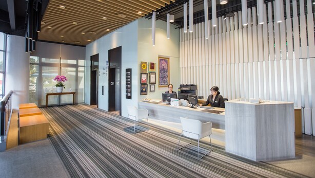A modern reception area with a reception desk, two chairs, a staircase, and a patterned carpet. - Jiuwu Hotel (Luodong)