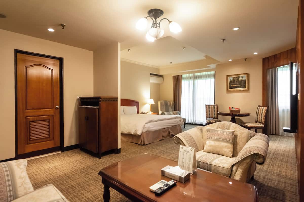 A hotel room with a bed, a sofa, a coffee table, a desk, and a door.
