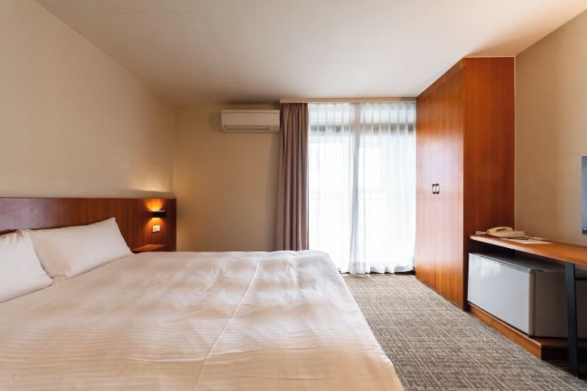 A hotel room with a large bed, a desk with a telephone, a television, and an air conditioning unit.