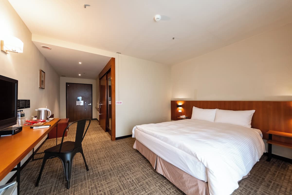 A hotel room with a bed, a desk with a chair, a television, and a door leading to another room.