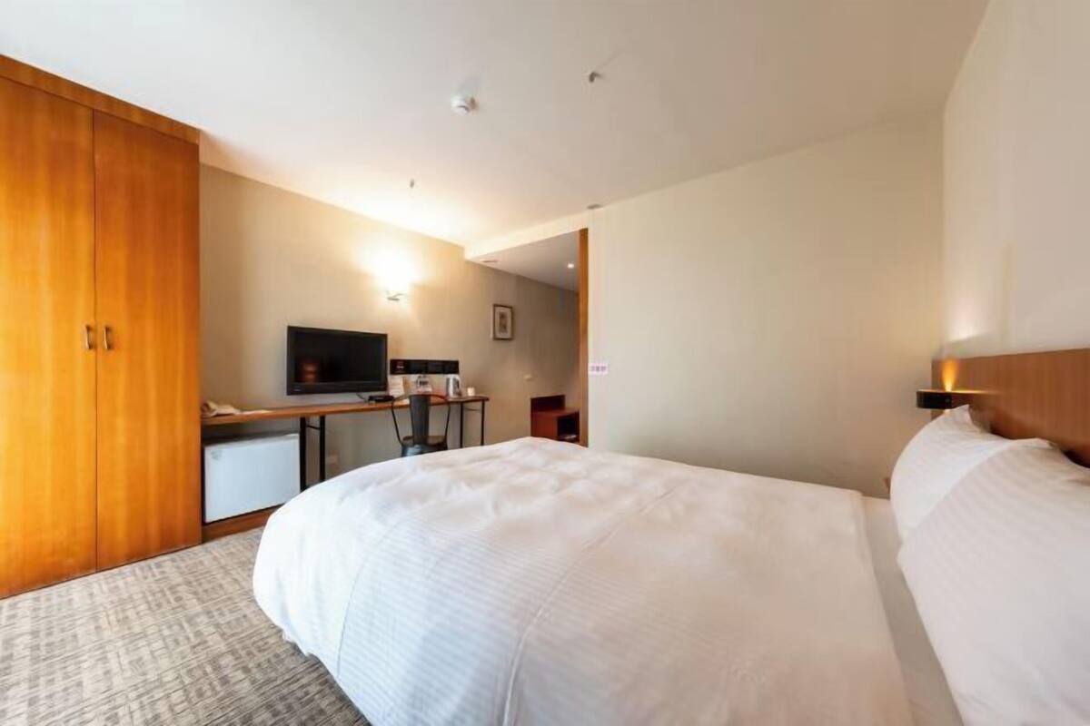 A hotel room with a bed, a desk with a computer, a television, and a wardrobe.