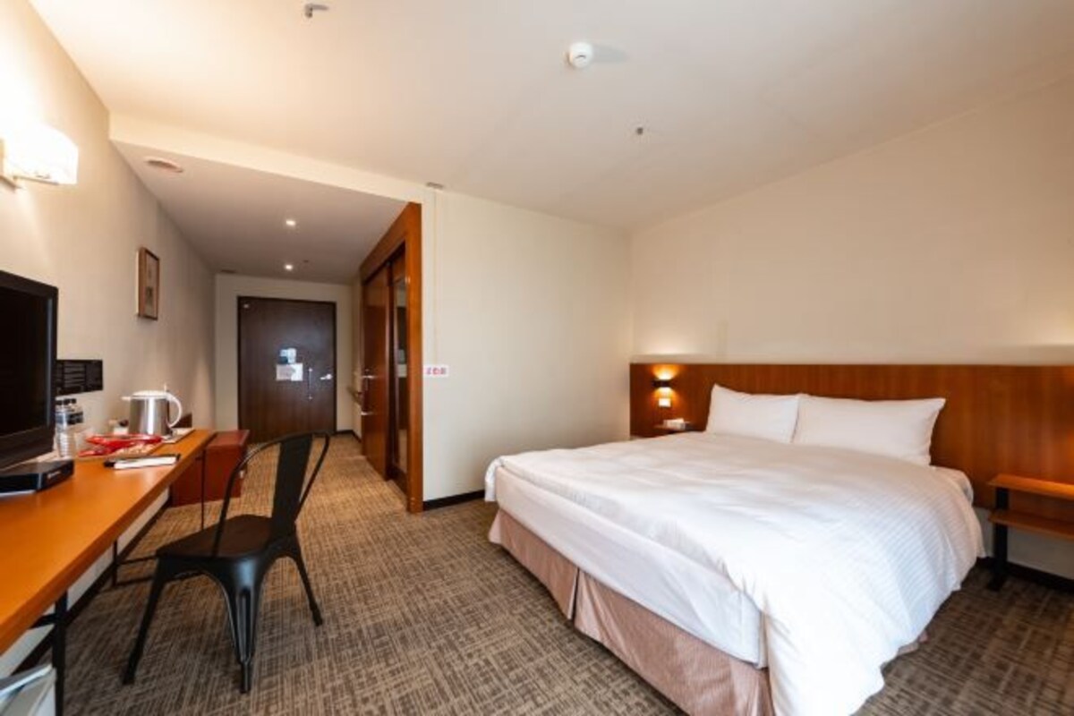 A hotel room with a bed, a desk with a chair, a television, and a door leading to another room.