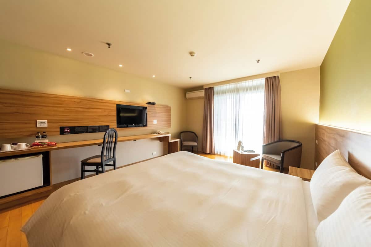 A hotel room with a large bed, a desk with a chair, a television, and a window with curtains.