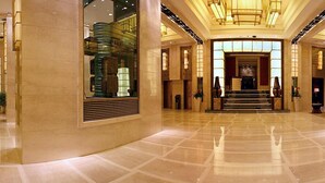 A spacious lobby with a polished marble floor, a central staircase, and a glass elevator. - Beijing Minzu Hotel    (Beijing)