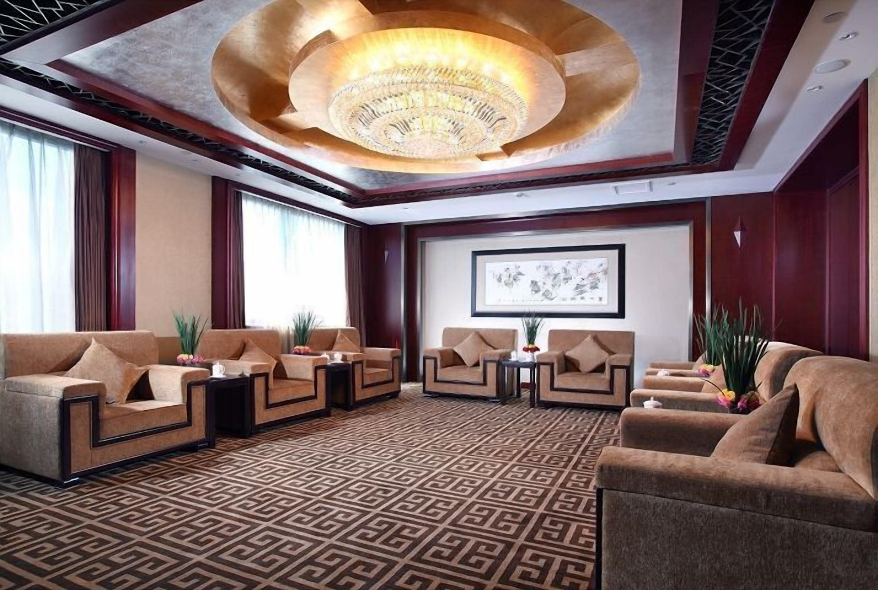 Ein großzügiger Lounge-Bereich mit in einer Halbkreisform angeordneten Sofas, einem gemusterten Teppich und einer großen Chandelier.