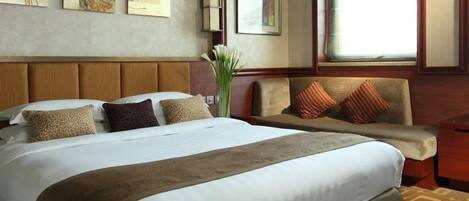 A hotel room with a large bed, a sofa, and a window with a view.