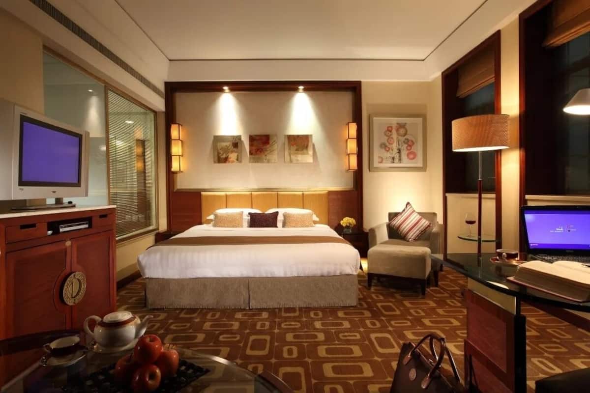 Une chambre d’hôtel avec un grand lit, un bureau avec un ordinateur portable, une télévision et une table basse avec des pommes.