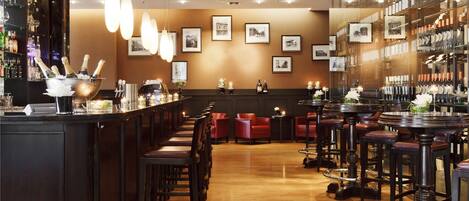 A bar area with wooden flooring, red leather chairs, and a bar counter with bottles and glasses.