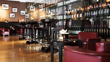 A bar area with multiple tables and chairs, a wine display, and framed pictures on the wall.