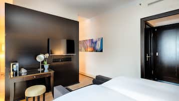Habitación de hotel con cama, escritorio, silla, televisión y un cuadro en la pared.