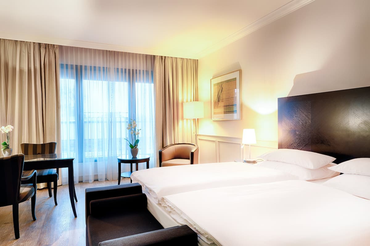 A hotel room with a large bed, a desk, two chairs, a small table, and a lamp.