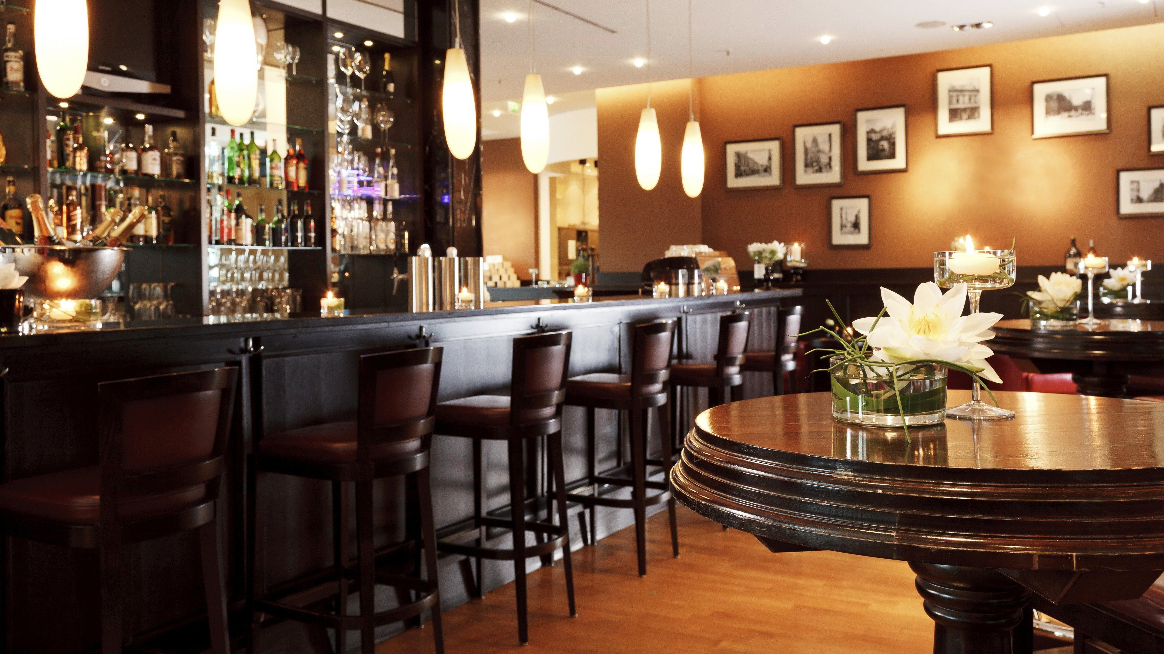 A bar area with a wooden bar counter, multiple bar stools, and a round table with a vase of flowers.
