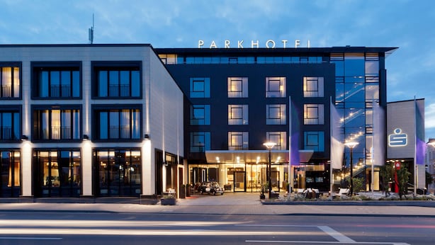 A modern hotel with a prominent 'Parkhotel' sign, large windows, and a well-lit entrance area. - Welcome Parkhotel Euskirchen (Euskirchen)