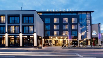 A modern hotel with a prominent 'Parkhotel' sign, large windows, and a well-lit entrance area.