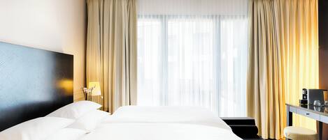 Una habitación de hotel con una cama grande, un escritorio con silla y una ventana con cortinas.