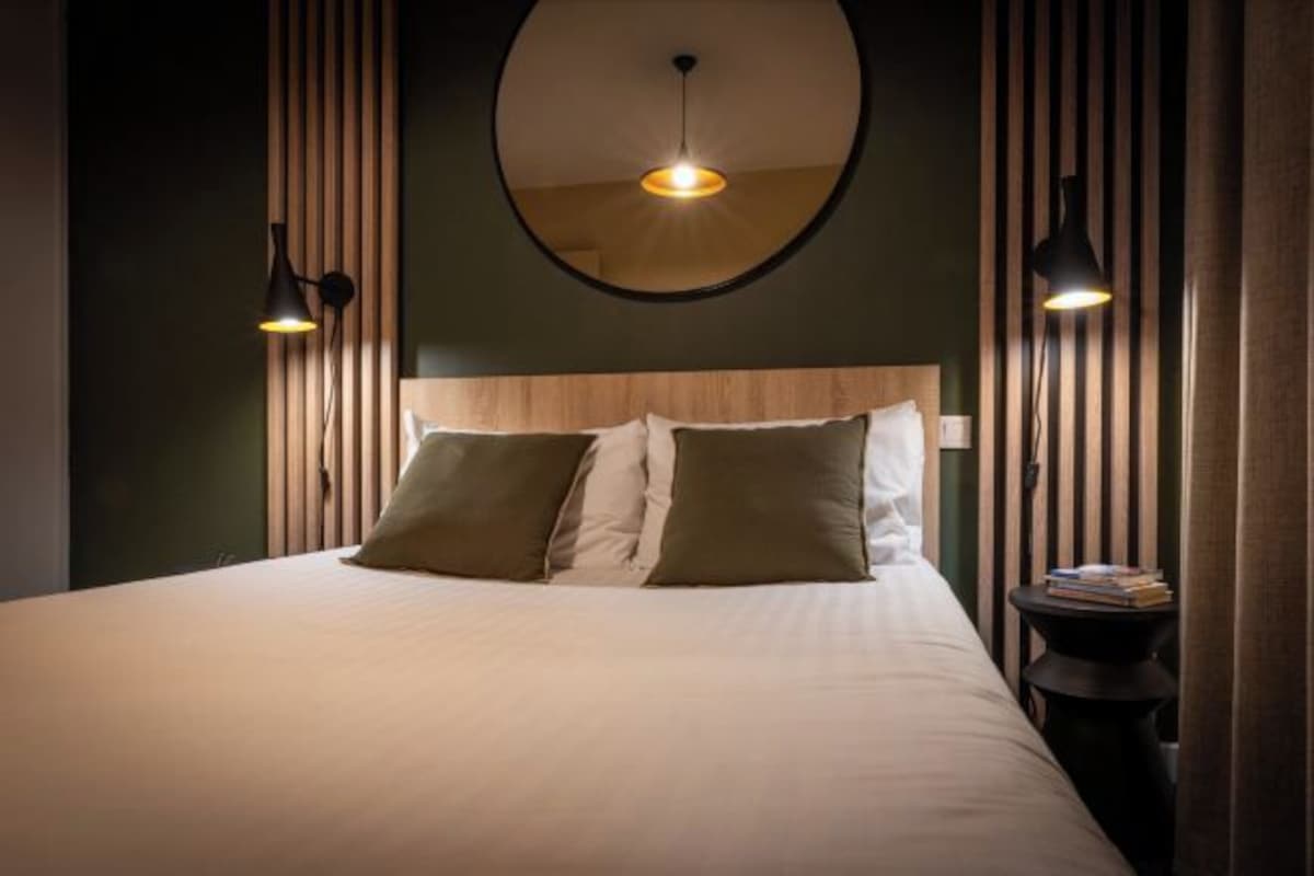 Una cama bien hecha con un cabecero, dos lámparas de noche y una mesita de noche con libros a su lado.