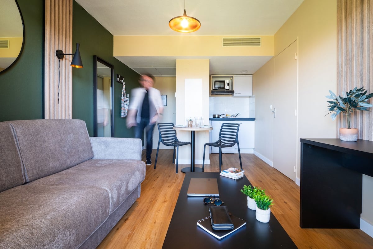 Una sala de estar moderna con un sofá, una mesa de centro con libros y una computadora portátil, y un comedor con sillas y una mesa.