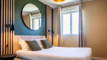 Une chambre d’hôtel avec un grand lit, un miroir rond, une table de chevet et une fenêtre avec des rideaux.