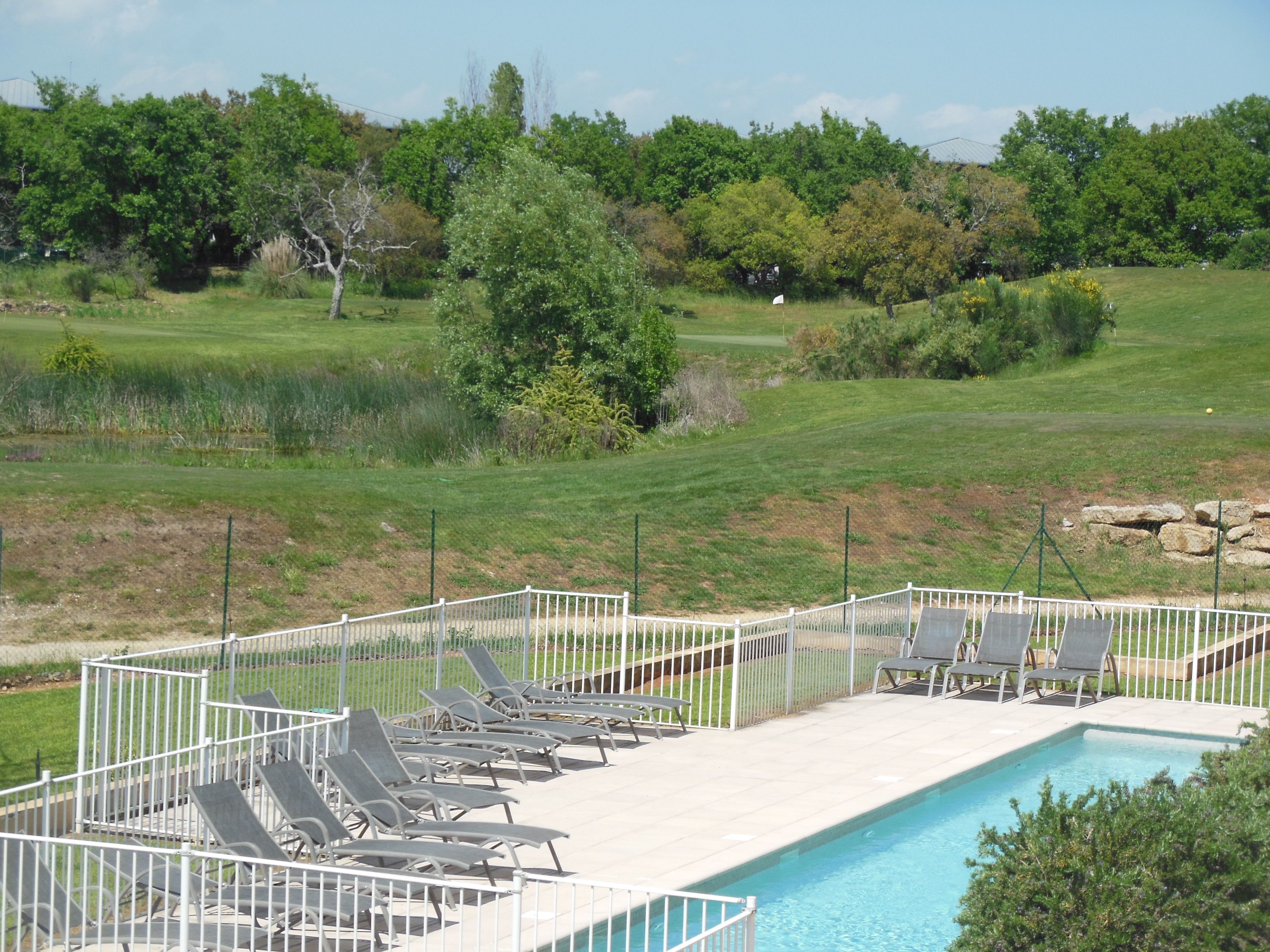 A pool area with lounge chairs and a view of a golf course.