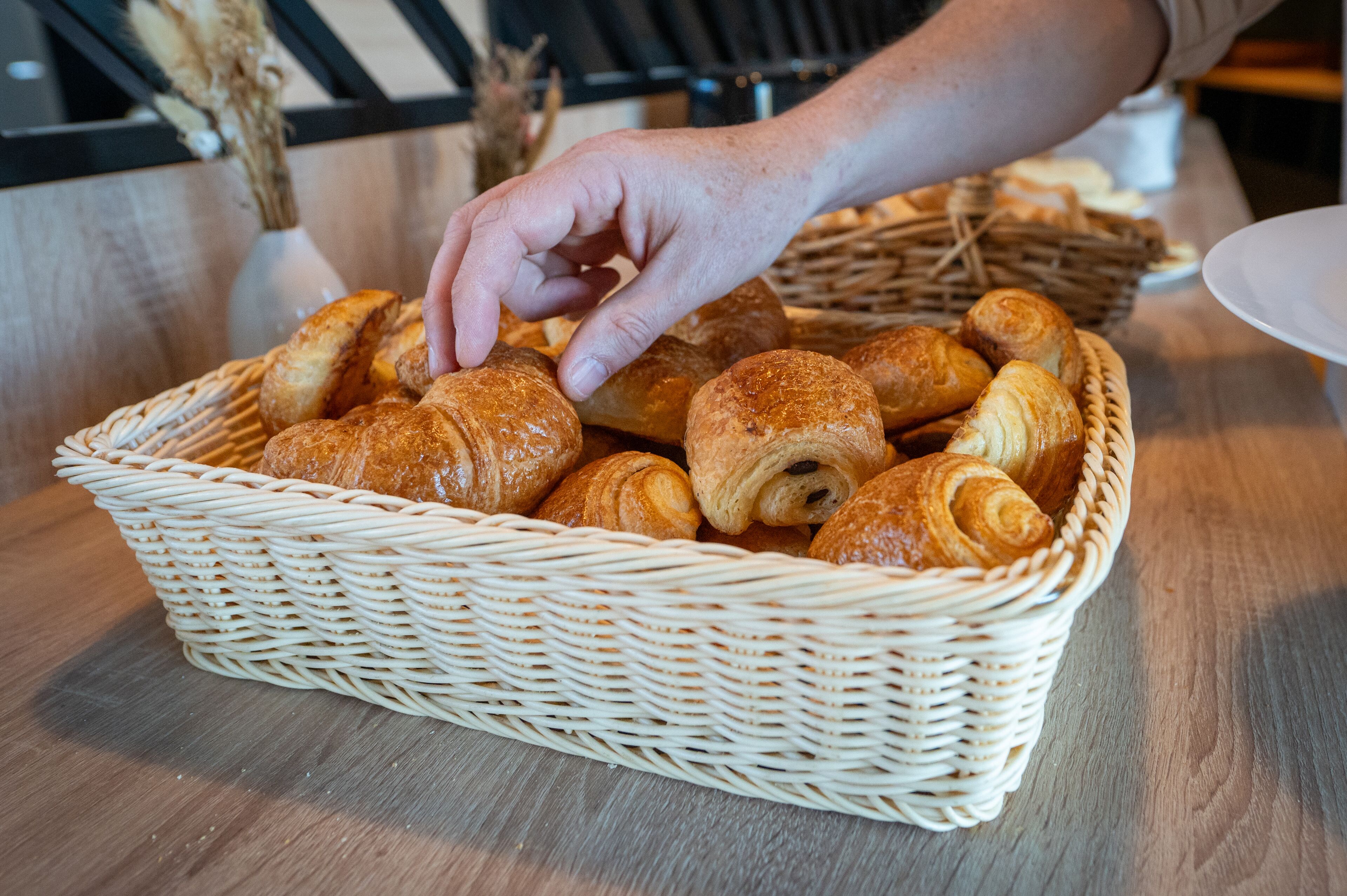 A wicker basket filled with various types of bread and pastries on a wooden table.