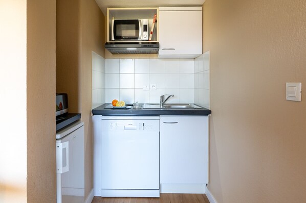 A compact kitchen with a microwave, dishwasher, and a small refrigerator. - Nemea Appart Hotel Green Side Biot Sophia Antipolis (Biot)