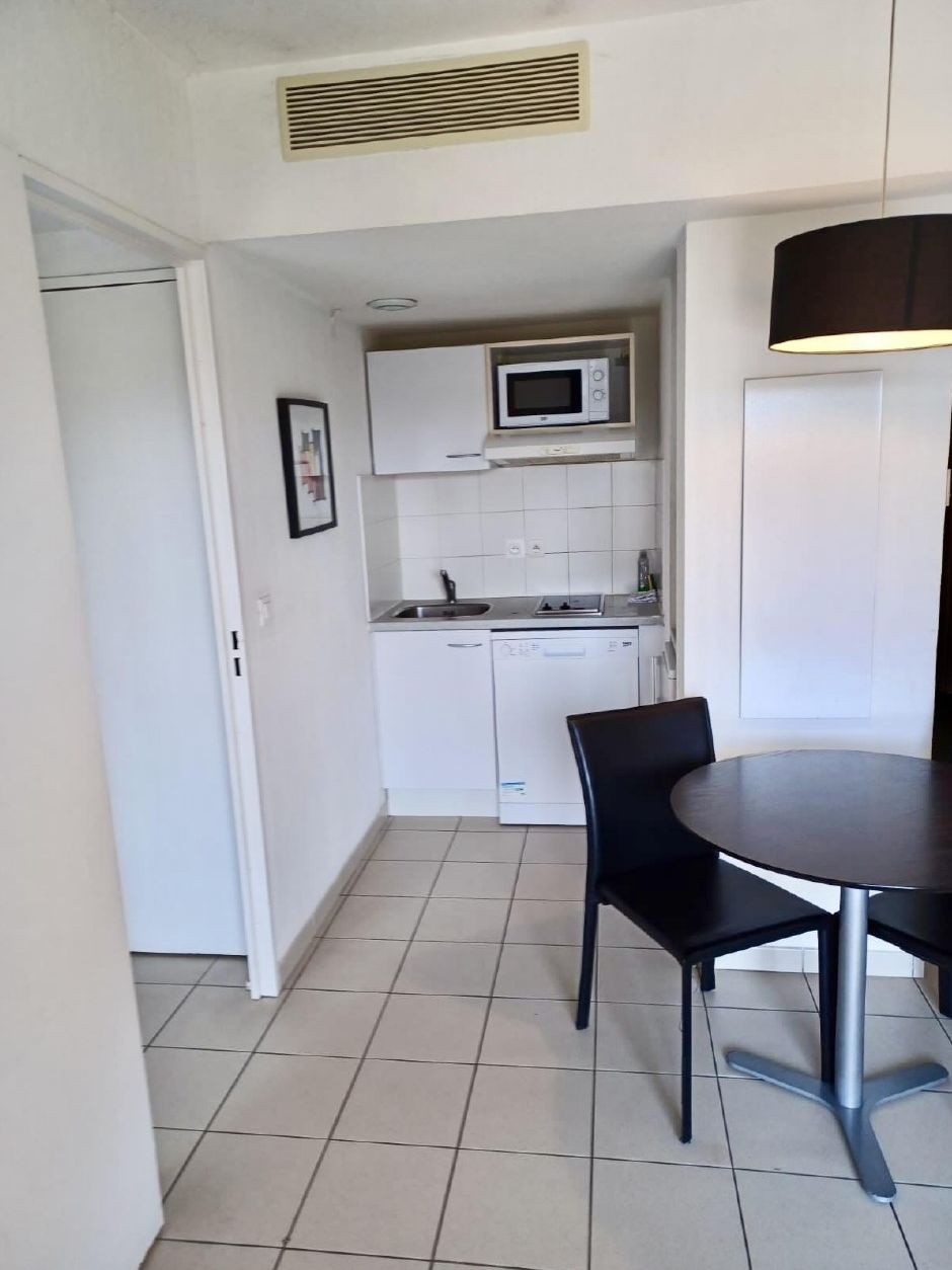 Cocina compacta con armarios blancos, microondas y pileta. Hay una mesa de comedor con sillas y una lámpara.