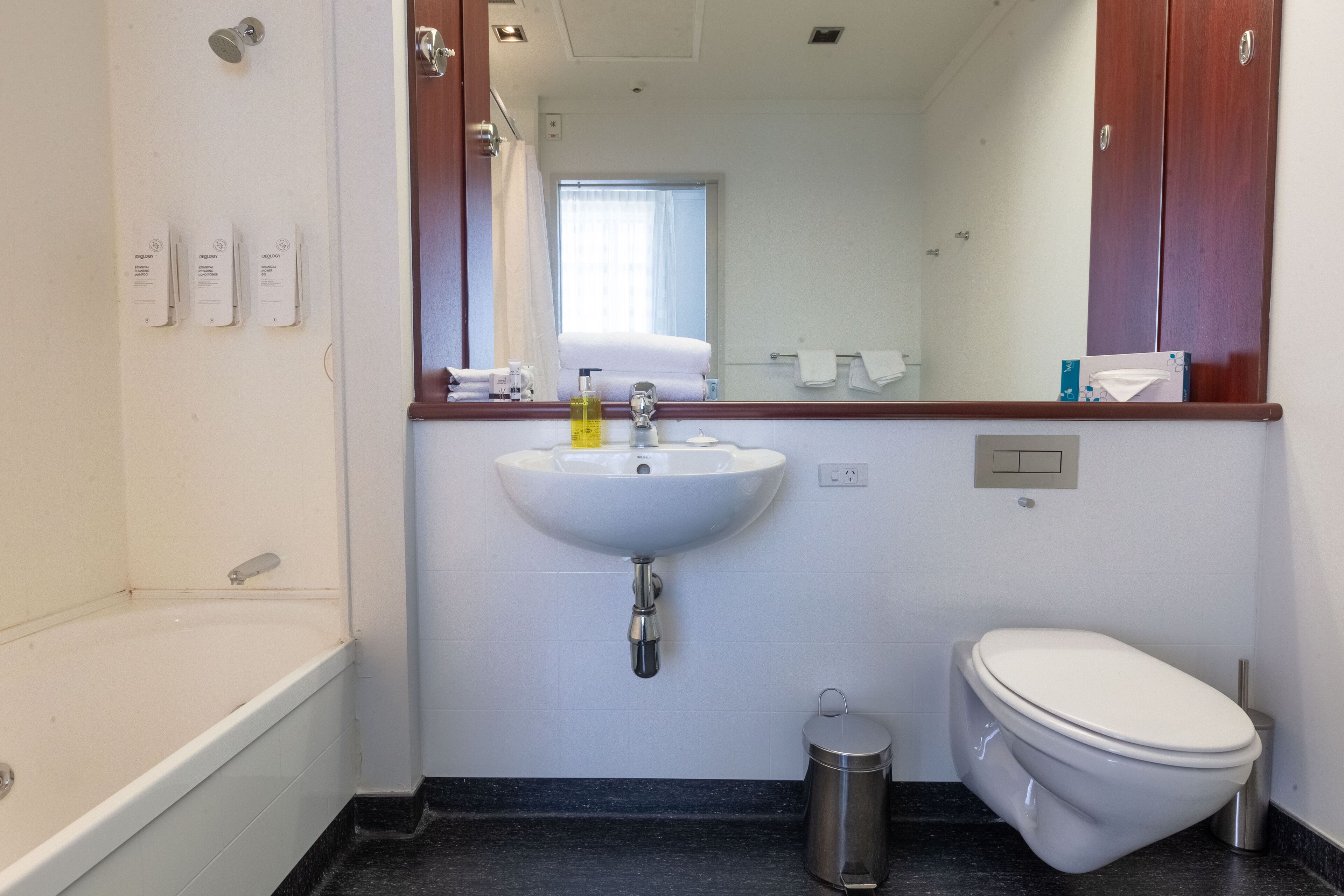 A bathroom with a white sink, a toilet, a trash can, and a mirror above the sink.