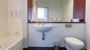 A bathroom with a white sink, a toilet, a trash can, and a mirror above the sink.