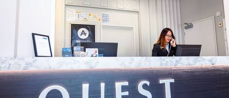 A reception desk with a sign reading "QUEST" and a person behind it.