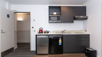 Cocina compacta con lavavajillas, microondas y hervidor sobre la encimera.