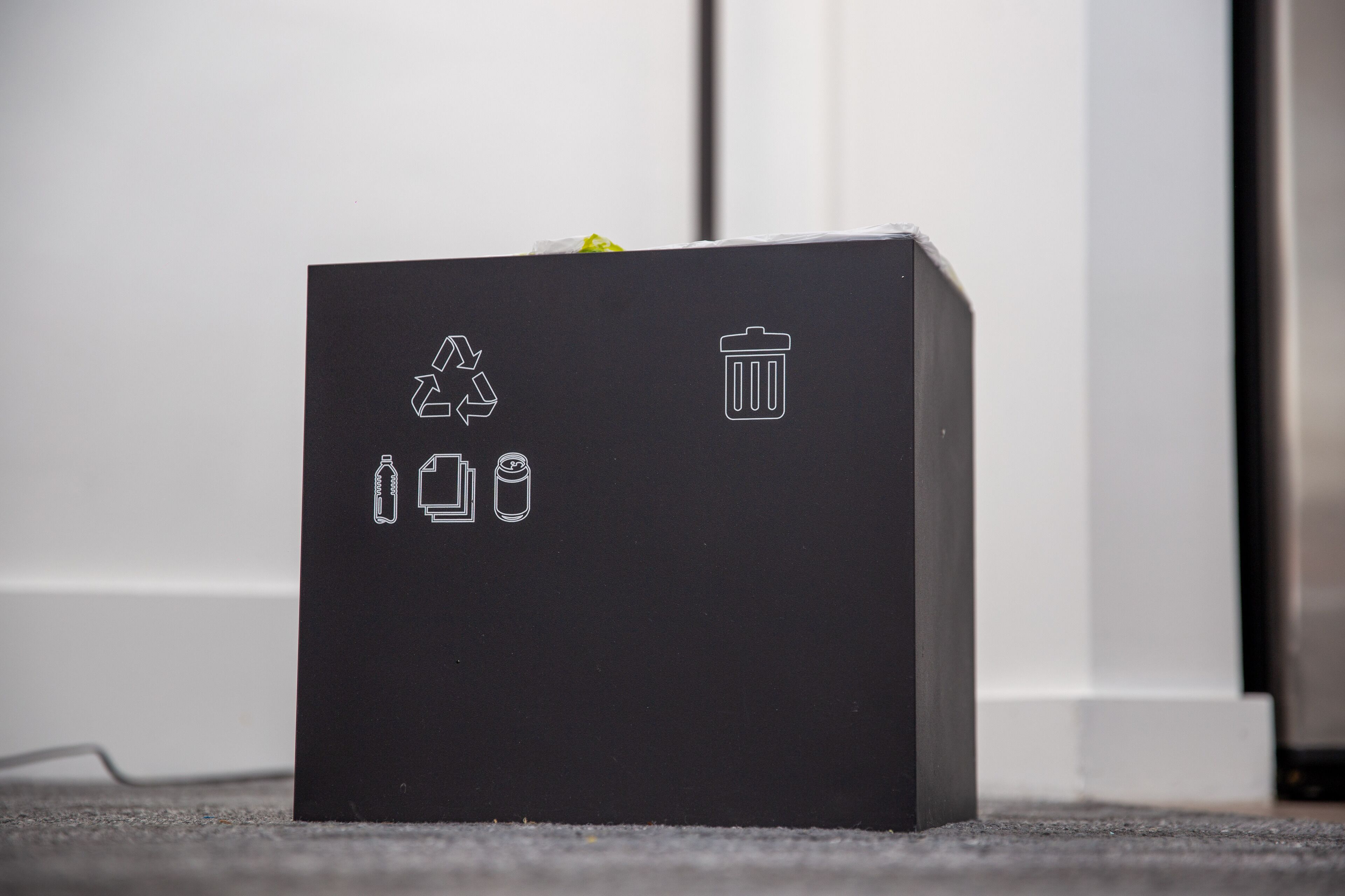 A black box with recycling and trash symbols on a carpeted floor.