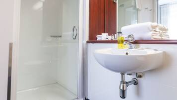 Un baño con ducha envuelta en vidrio, un lavabo blanco y un espejo encima.