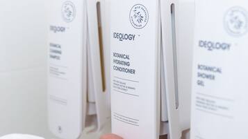 Una mano sostiene un dispensador blanco con la etiqueta 'Ideology Botanical Hydrating Conditioner'.