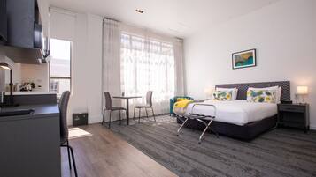 A hotel room with a bed, a desk, a chair, a small table, and a window with curtains.