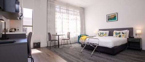 A hotel room with a bed, a desk, a chair, a small table, and a window with curtains.