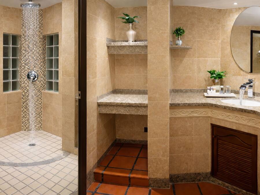 Un baño con ducha, lavamanos, espejo y planta en maceta.